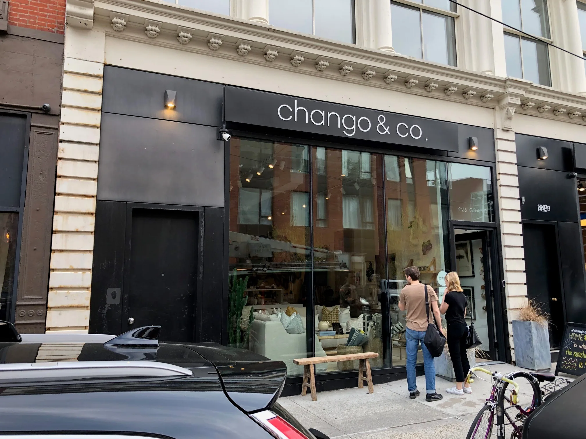 Flat black fascia sign with white lettering lit by small lamps above a glass storefront