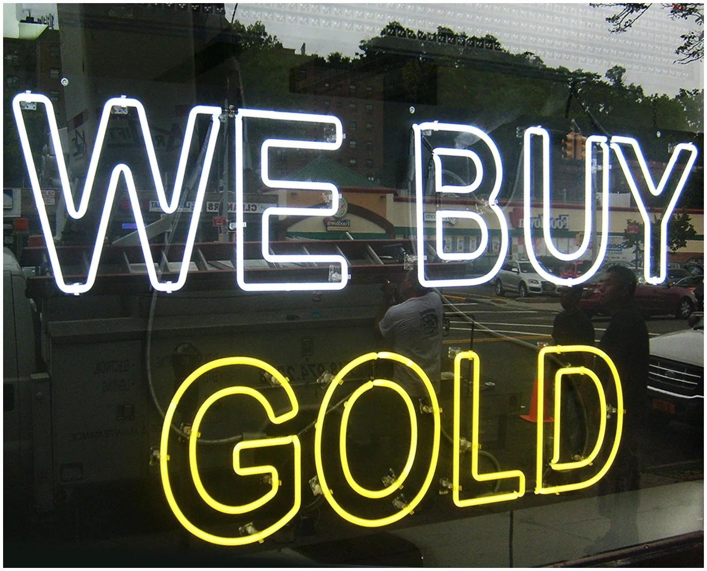 White and yellow neon window sign reading We Buy Gold glowing behind the glass