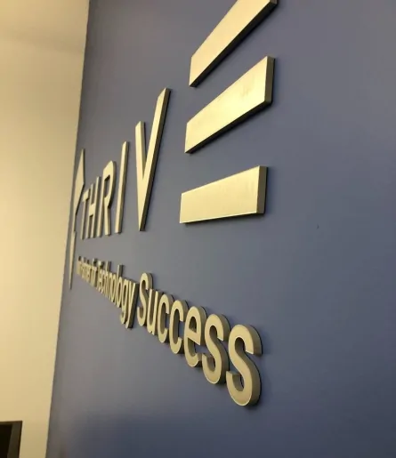 Gold finish dimensional lettering for Thrive on a dark painted wall