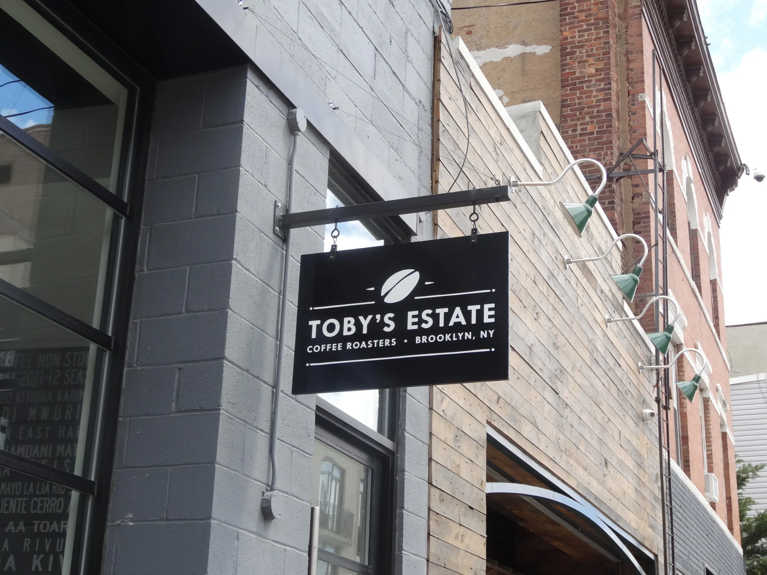 Black blade sign with a coffee bean logo hanging from a bracket on a gray block storefront