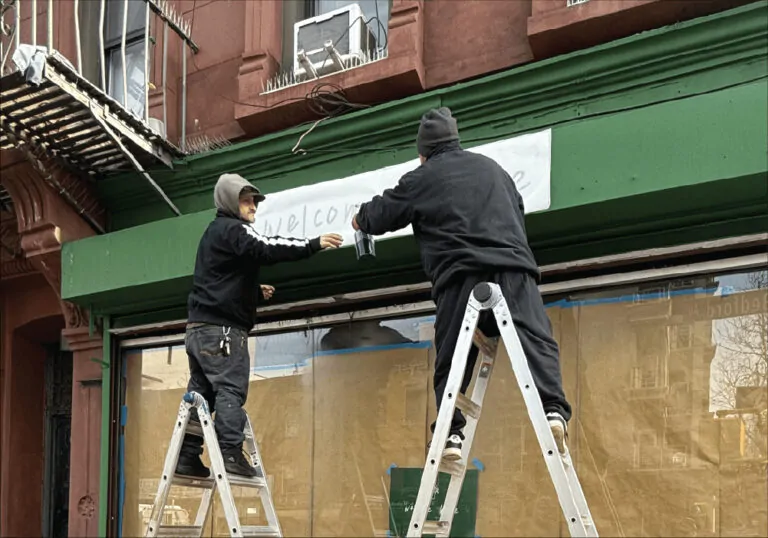 Sign painters hand lettering a storefront fascia on site