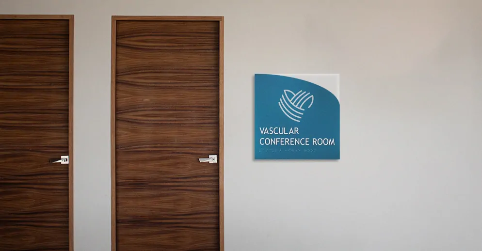Blue curved wall sign reading Vascular Conference Room mounted beside a timber office door