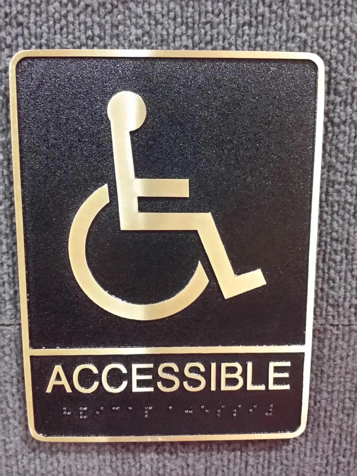 Black and gold accessible sign with the wheelchair symbol raised letters and braille