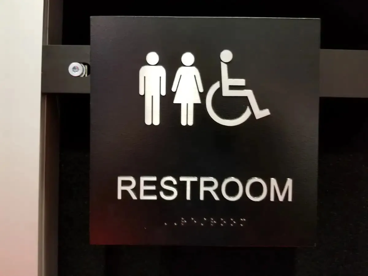 Black restroom sign with raised pictograms raised letters and braille