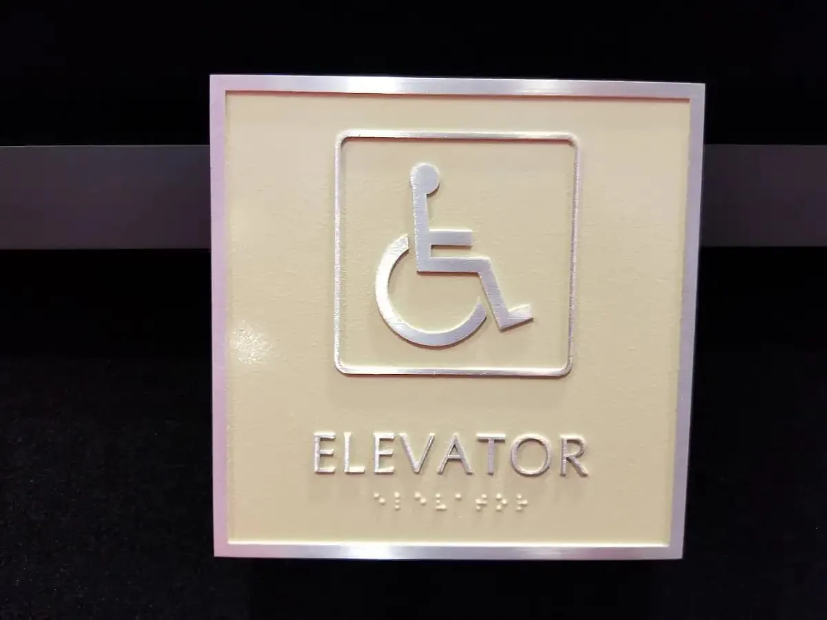 Cream tactile elevator sign with the accessibility symbol and braille