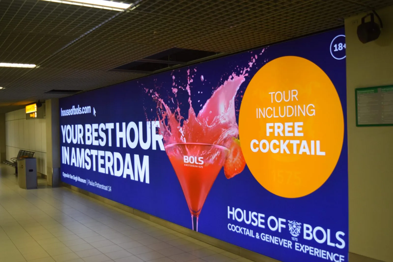 Large backlit wall graphic with a red cocktail and bold white type along an airport corridor