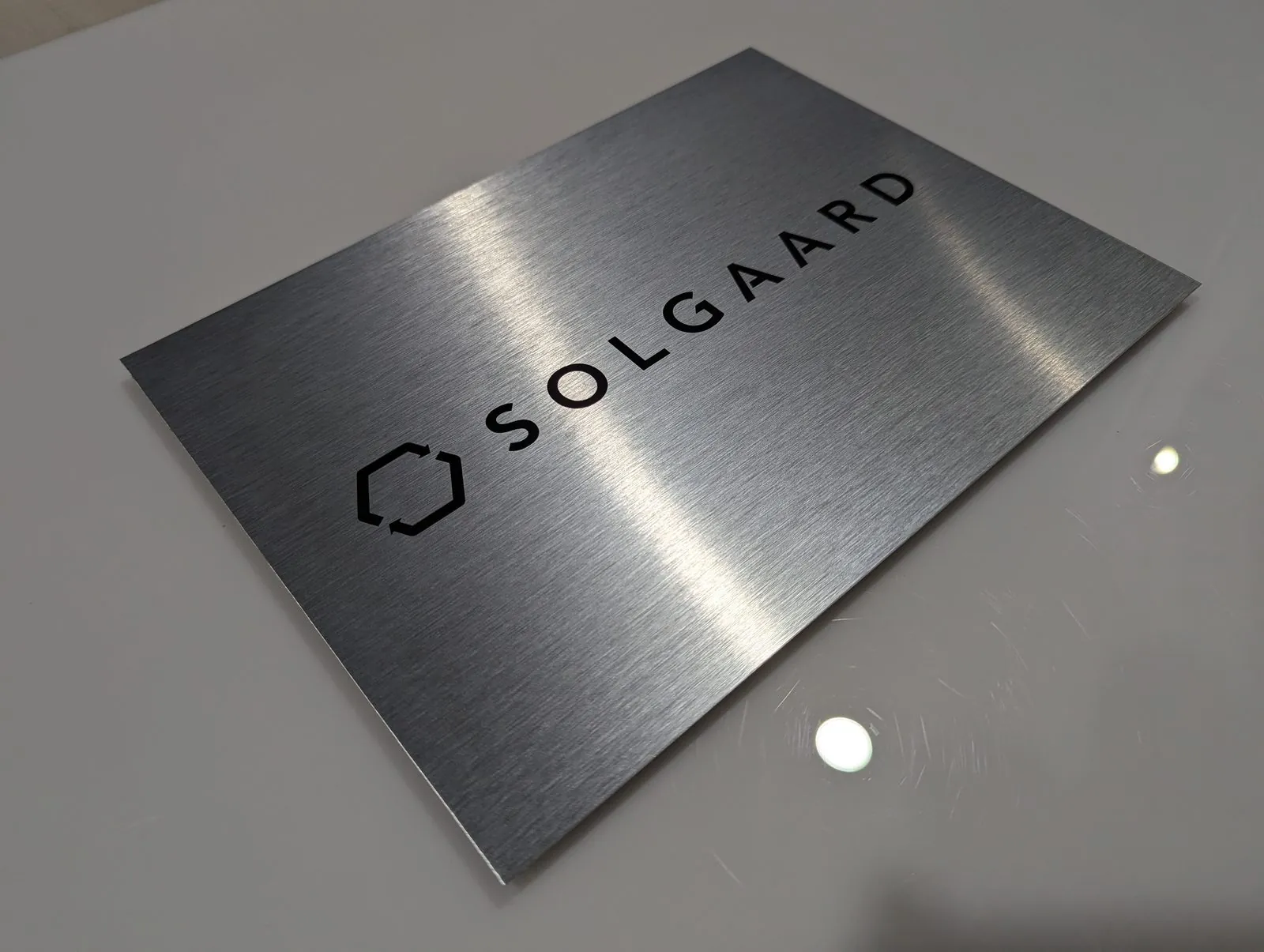 Brushed aluminum panel with a black cut vinyl logo and spaced company name