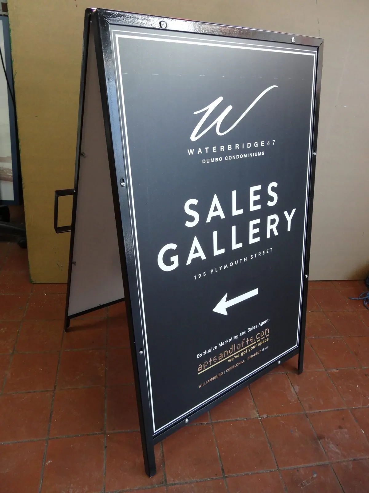 Black metal A frame sign with a white logo, the words Sales Gallery and an arrow
