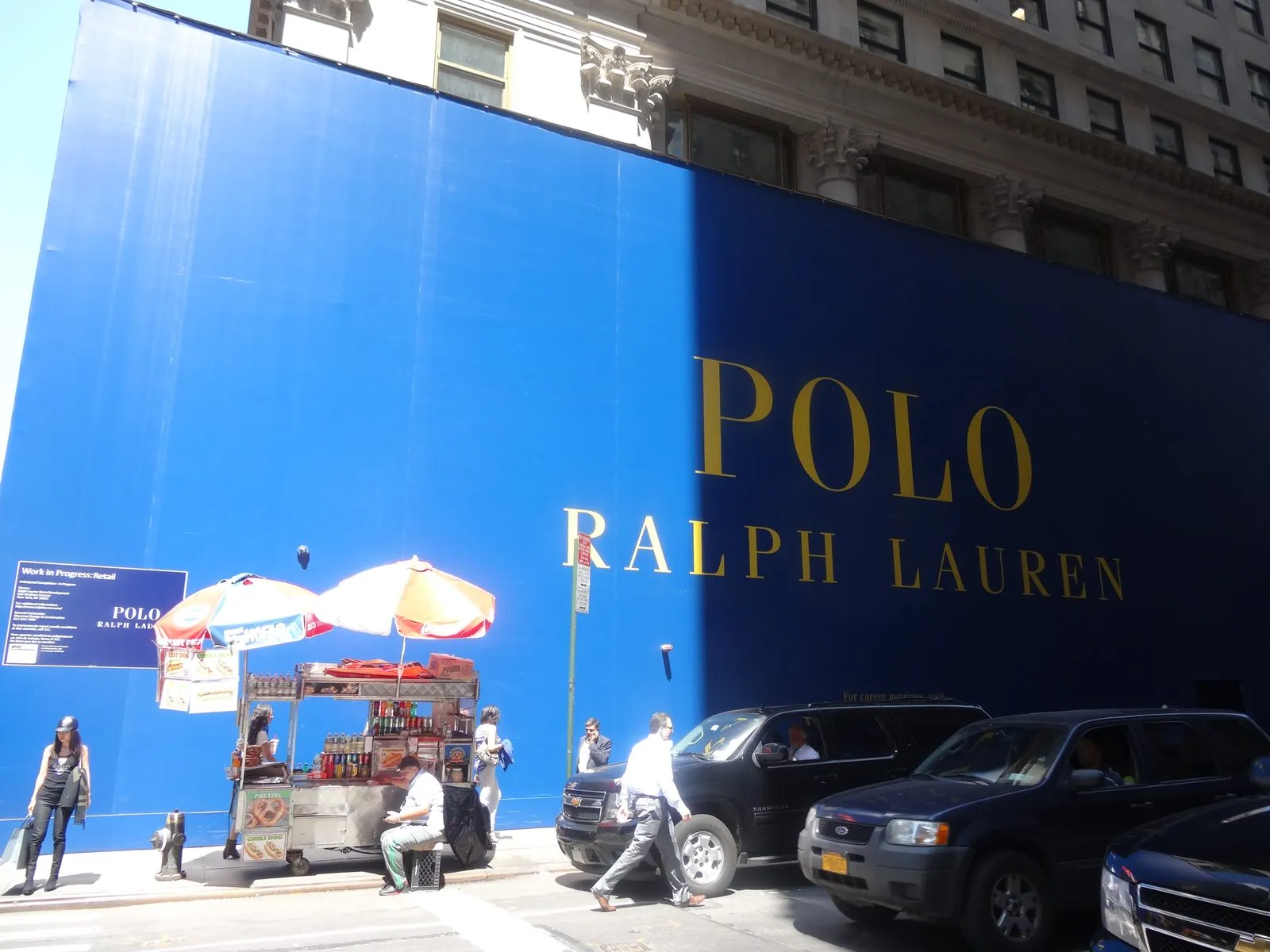 Blue barricade wall with gold store lettering along a city sidewalk