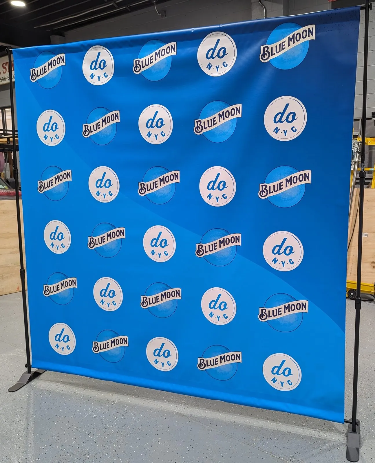 Blue step and repeat backdrop with round white logos in a grid, standing on a frame