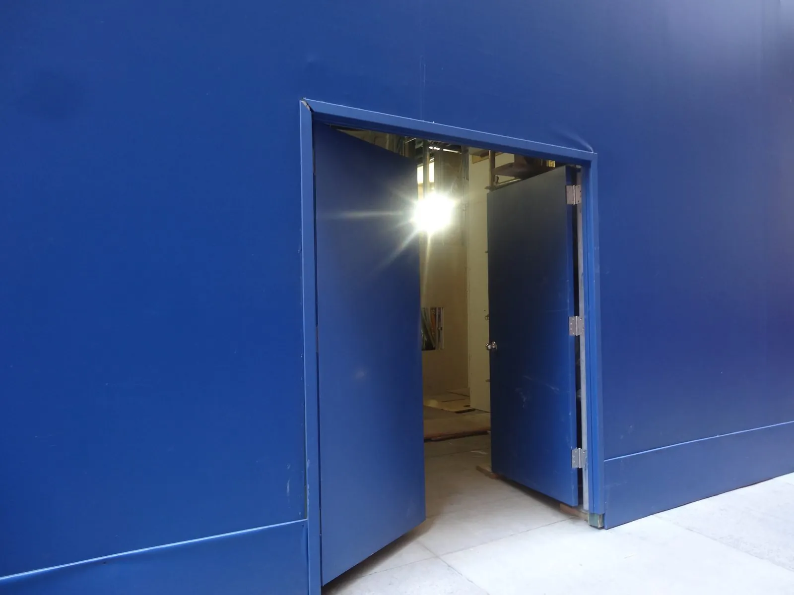 Blue printed barricade wall on a sidewalk with a door built into it standing open