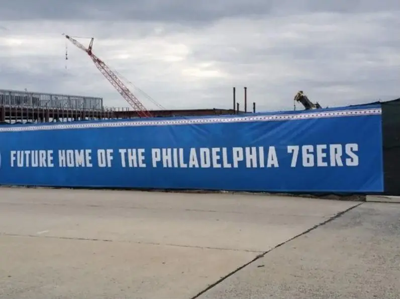 Blue mesh banner reading Future Home of the Philadelphia 76ers on a construction site fence