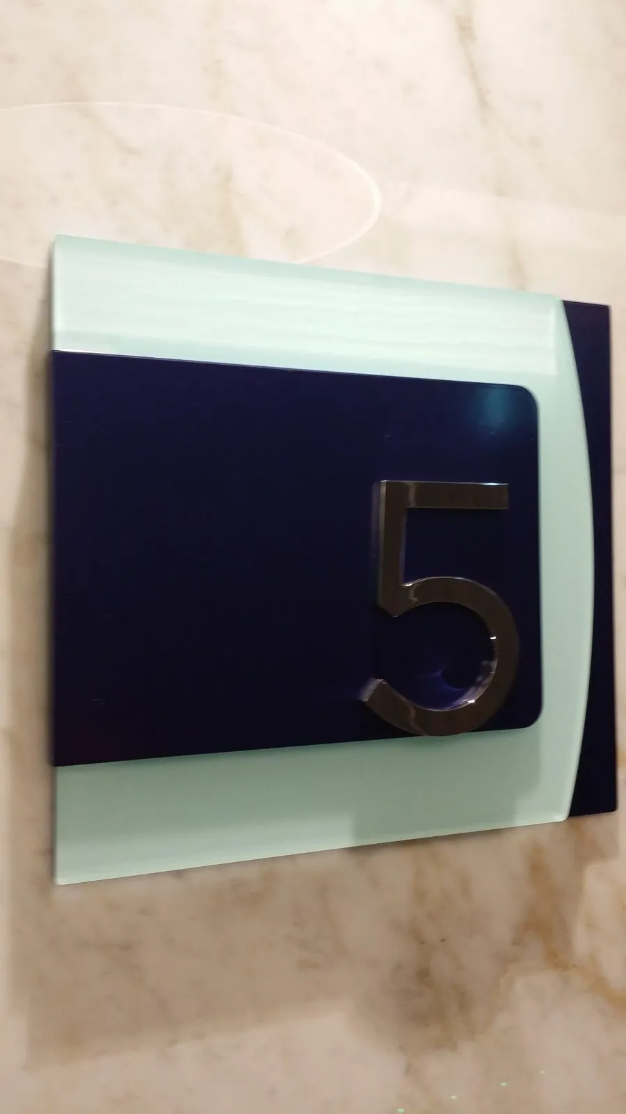 Polished metal number 5 on a layered navy and frosted acrylic panel on a marble wall