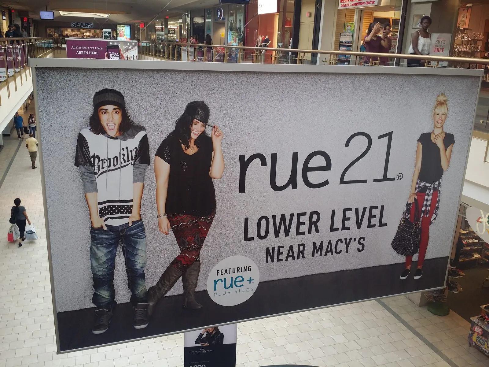 Large framed graphic hanging over a mall atrium, pointing shoppers to a store on the lower level