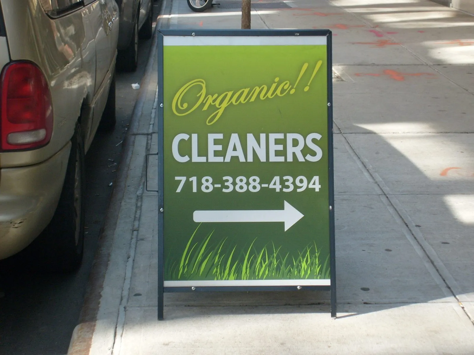 Green metal A frame sign reading Organic Cleaners with a phone number and an arrow on a sidewalk