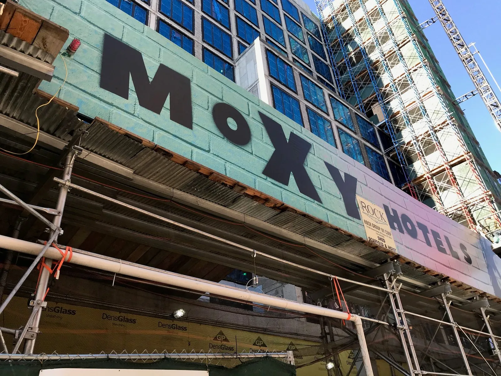 Big hotel name in black letters on a green scaffold banner over a sidewalk shed