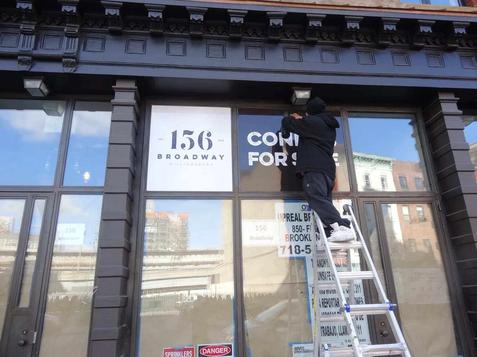Installer on a ladder applying white lettering panels to a storefront window