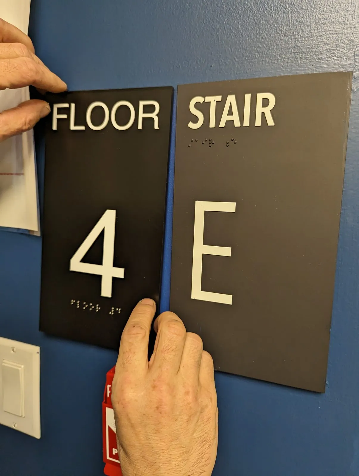 Installer pressing a Floor 4 sign into place next to a Stair E sign on a blue wall