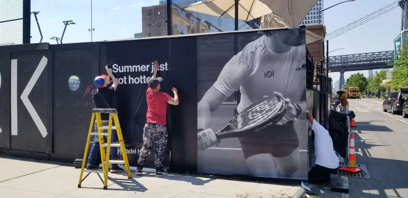 Two installers on a ladder smoothing a printed wrap onto a black fence panel