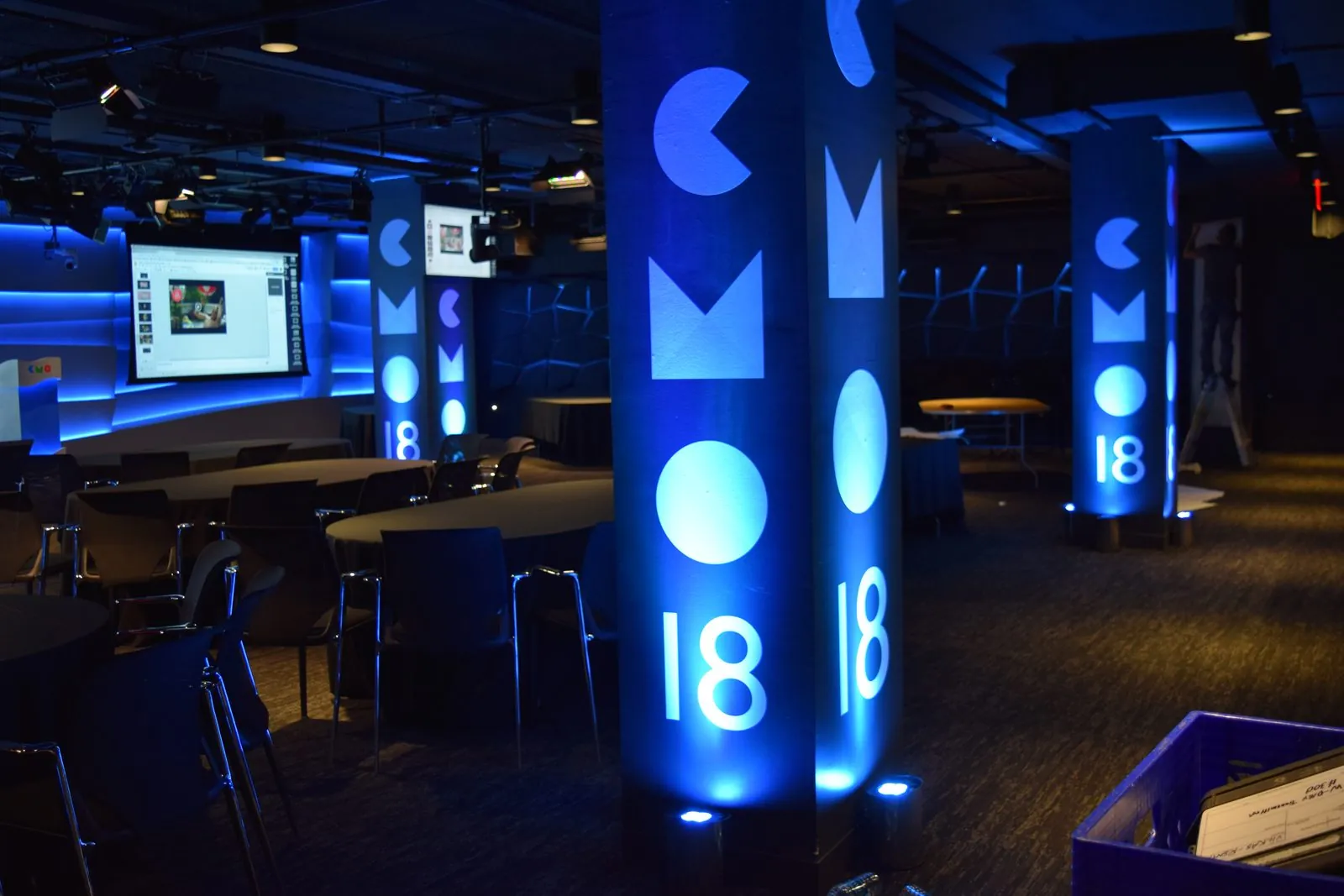 Tall printed column covers with bold shapes and the number 18, lit blue in an evening event space