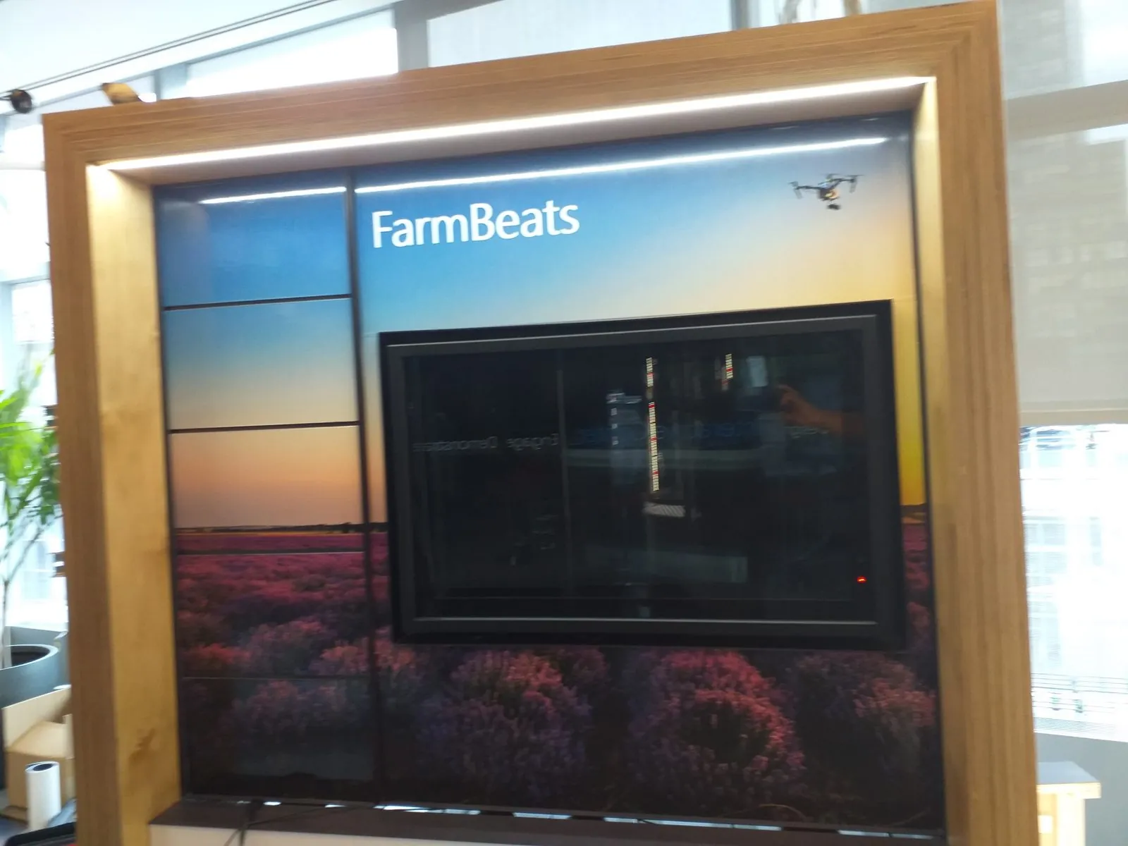 Wood frame with a built in light strip around a printed sunset field graphic and a screen in an office