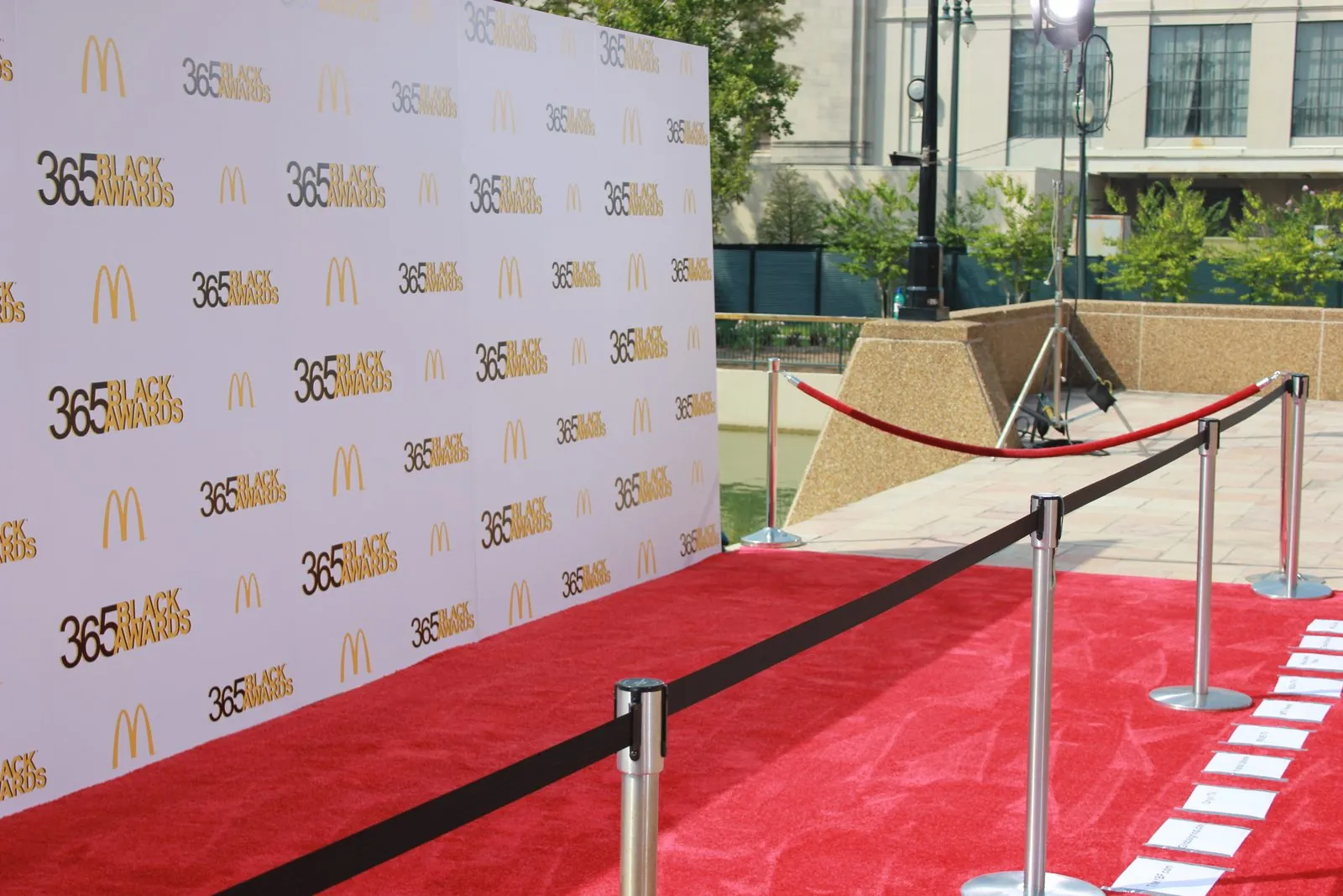 White logo wall with gold logos, a red carpet and silver stanchions set up at an outdoor venue