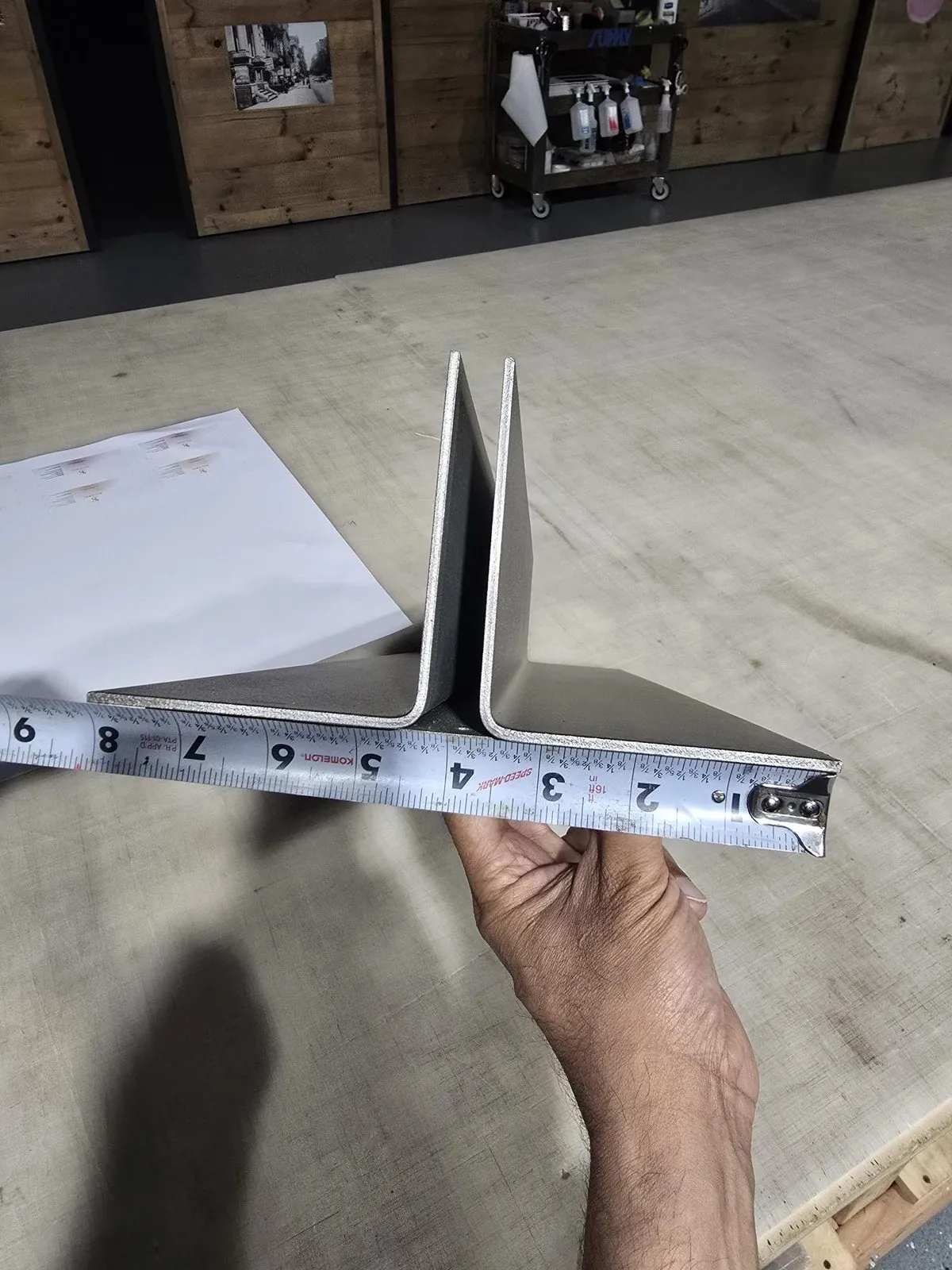 Hand holding a tape measure across an aluminum frame profile on the shop table