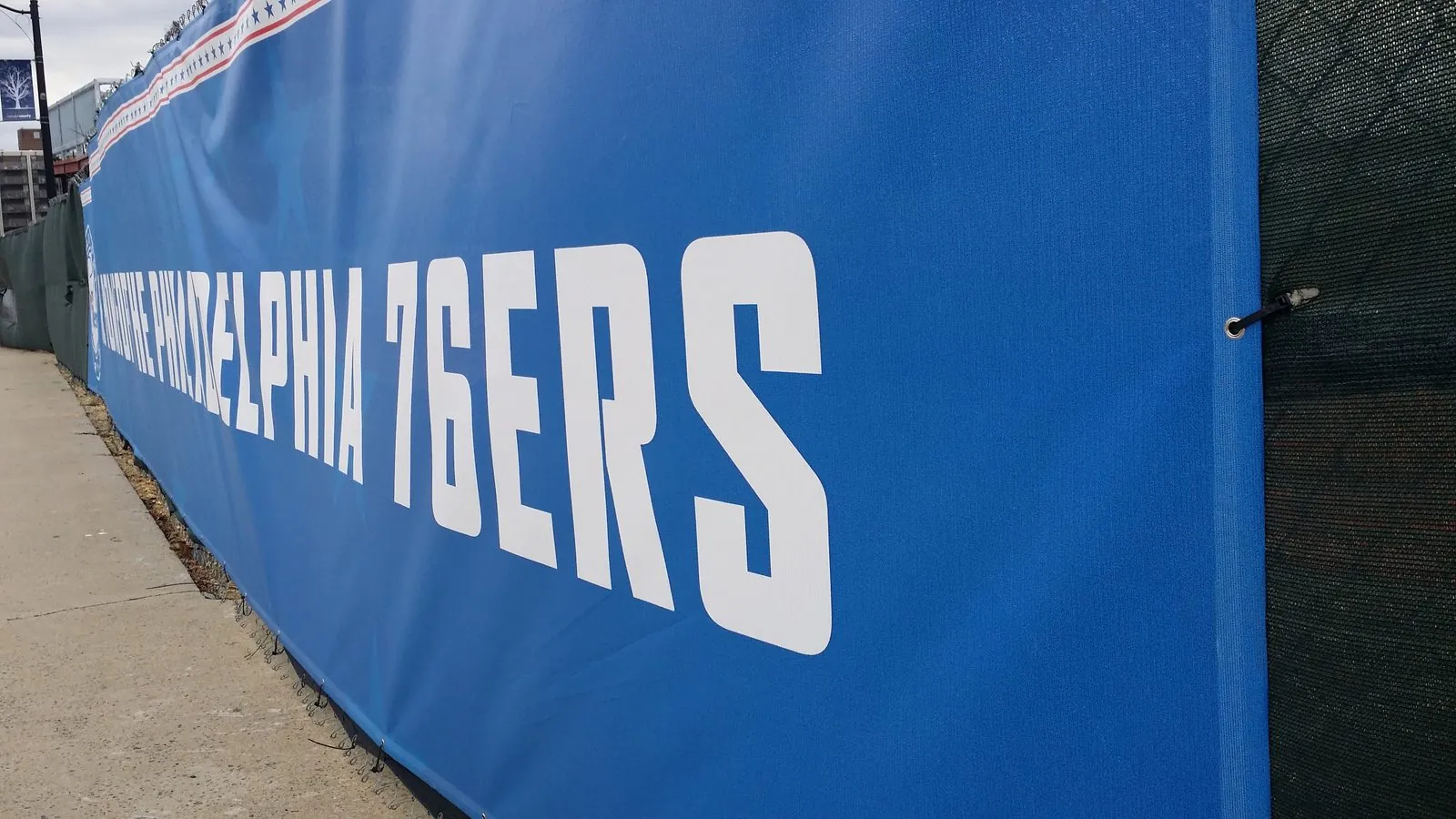 Blue mesh banner tied through its grommets to a chain link construction fence