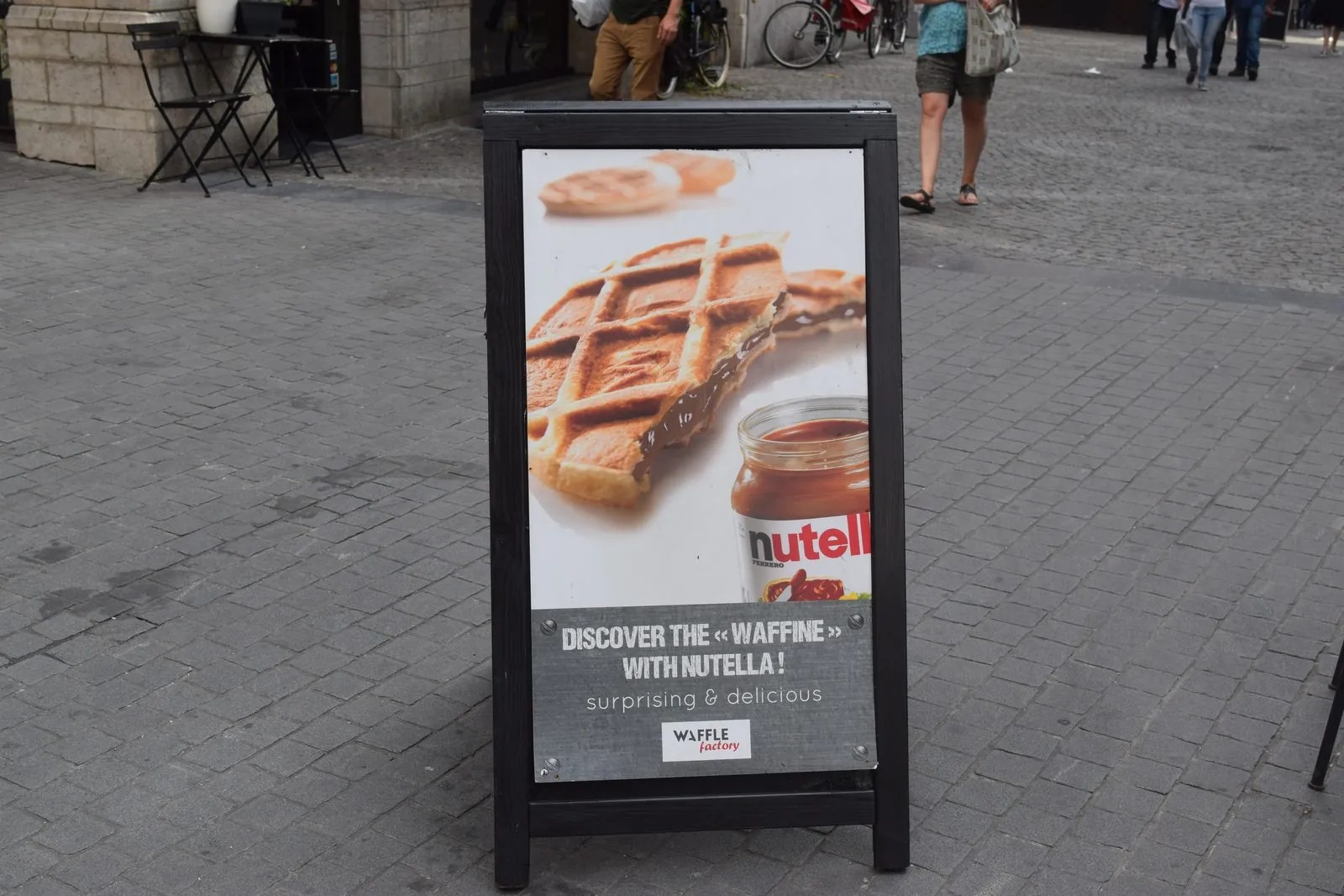 Black metal A frame sidewalk sign with a waffle poster on a city plaza