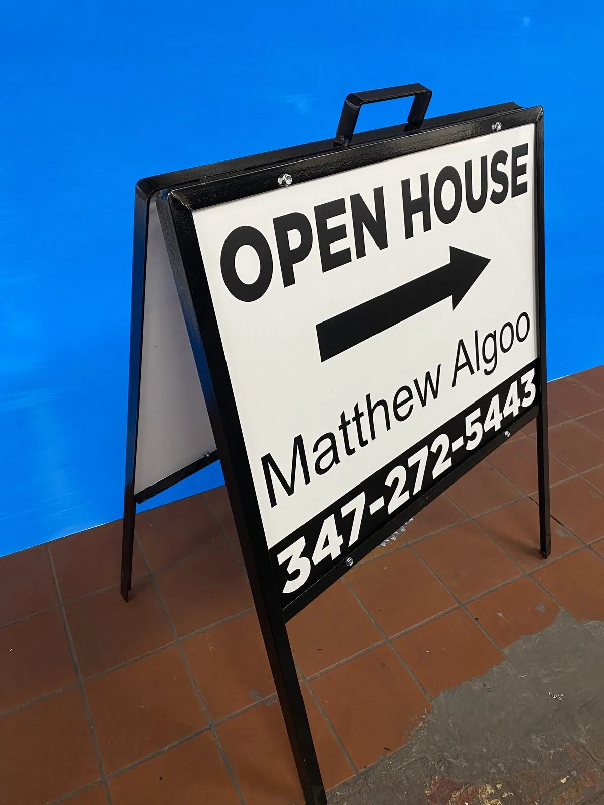 Black A frame open house sign with an arrow and a phone number on a sidewalk