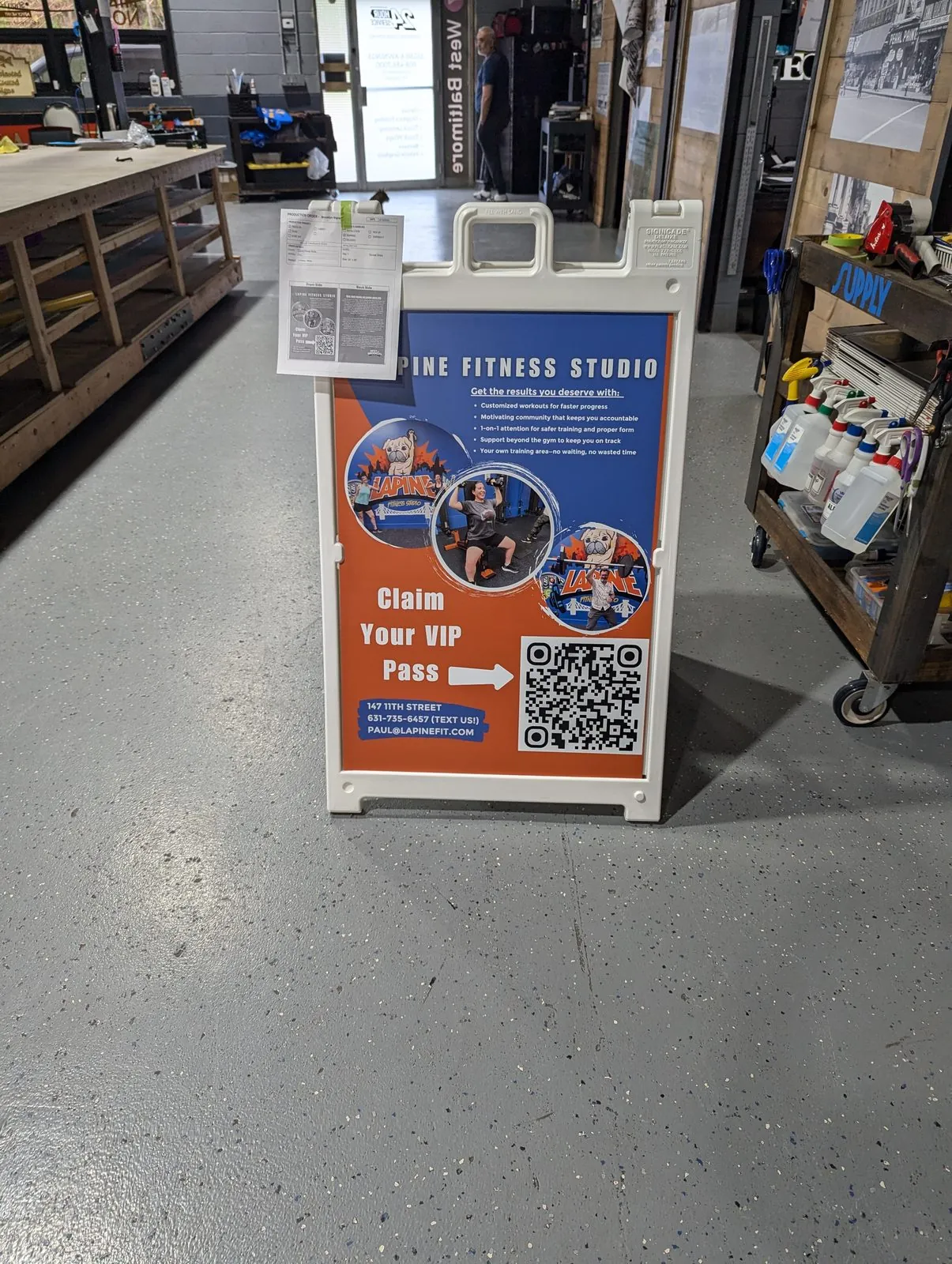 White plastic sandwich board with an orange fitness studio poster and a QR code