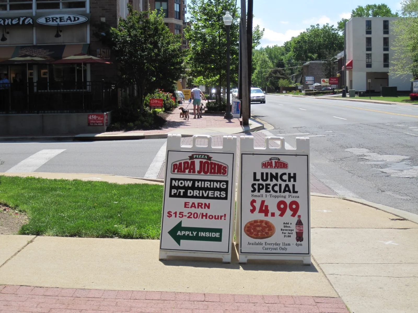 Two white plastic sandwich boards with pizza shop hiring and lunch special signs on a corner sidewalk