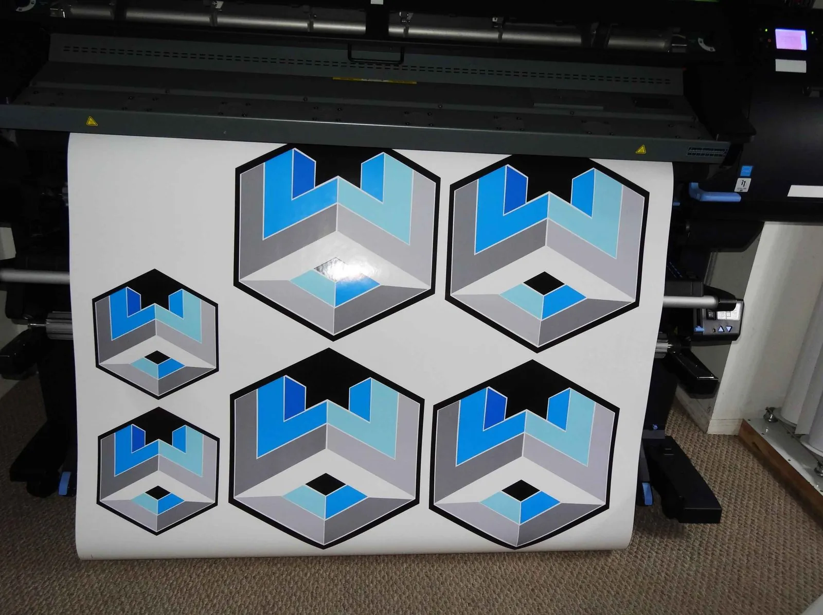 Roll of printed hexagon logo decals coming off a wide format printer