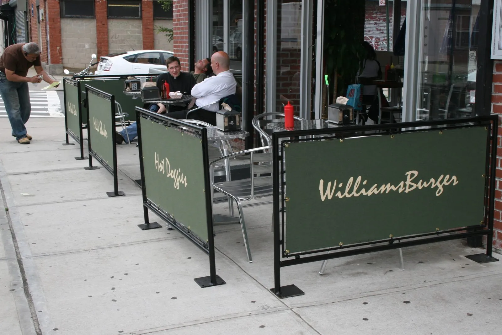 Row of printed green cafe barriers around outdoor tables on a sidewalk