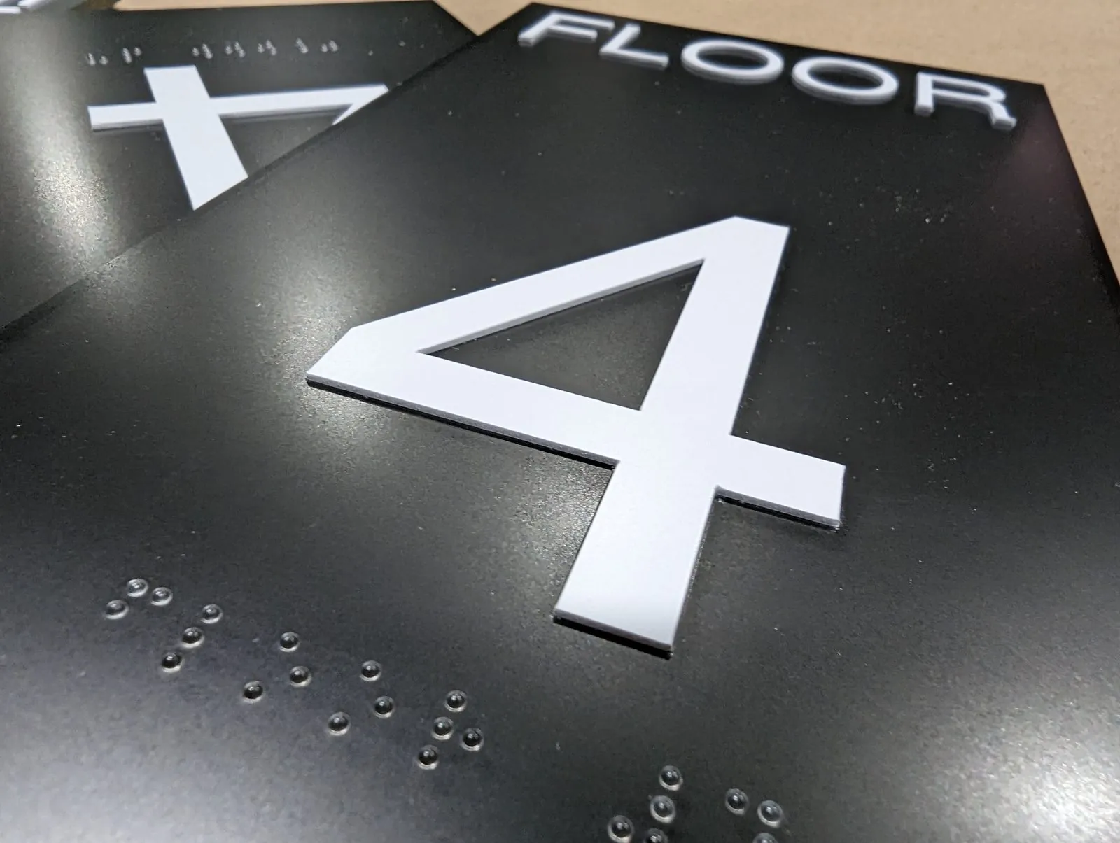 Close up of a raised white number 4 and braille dots on a black floor sign