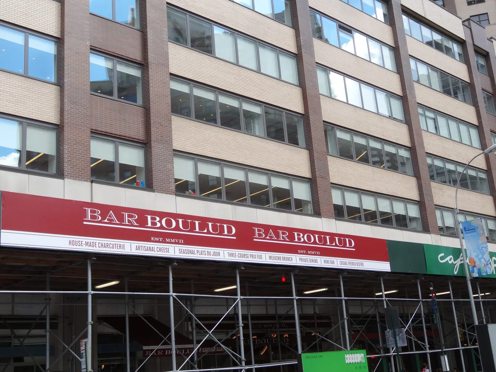 Red printed banner along a sidewalk shed in front of a mid rise building