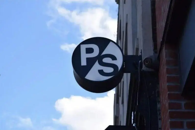 Round blade sign with a simple two letter logo against a blue sky