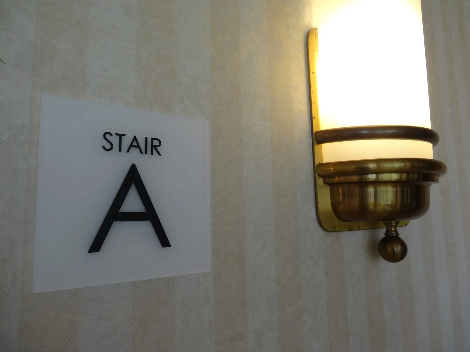 White Stair A sign with black letters on a striped hallway wall beside a brass wall light