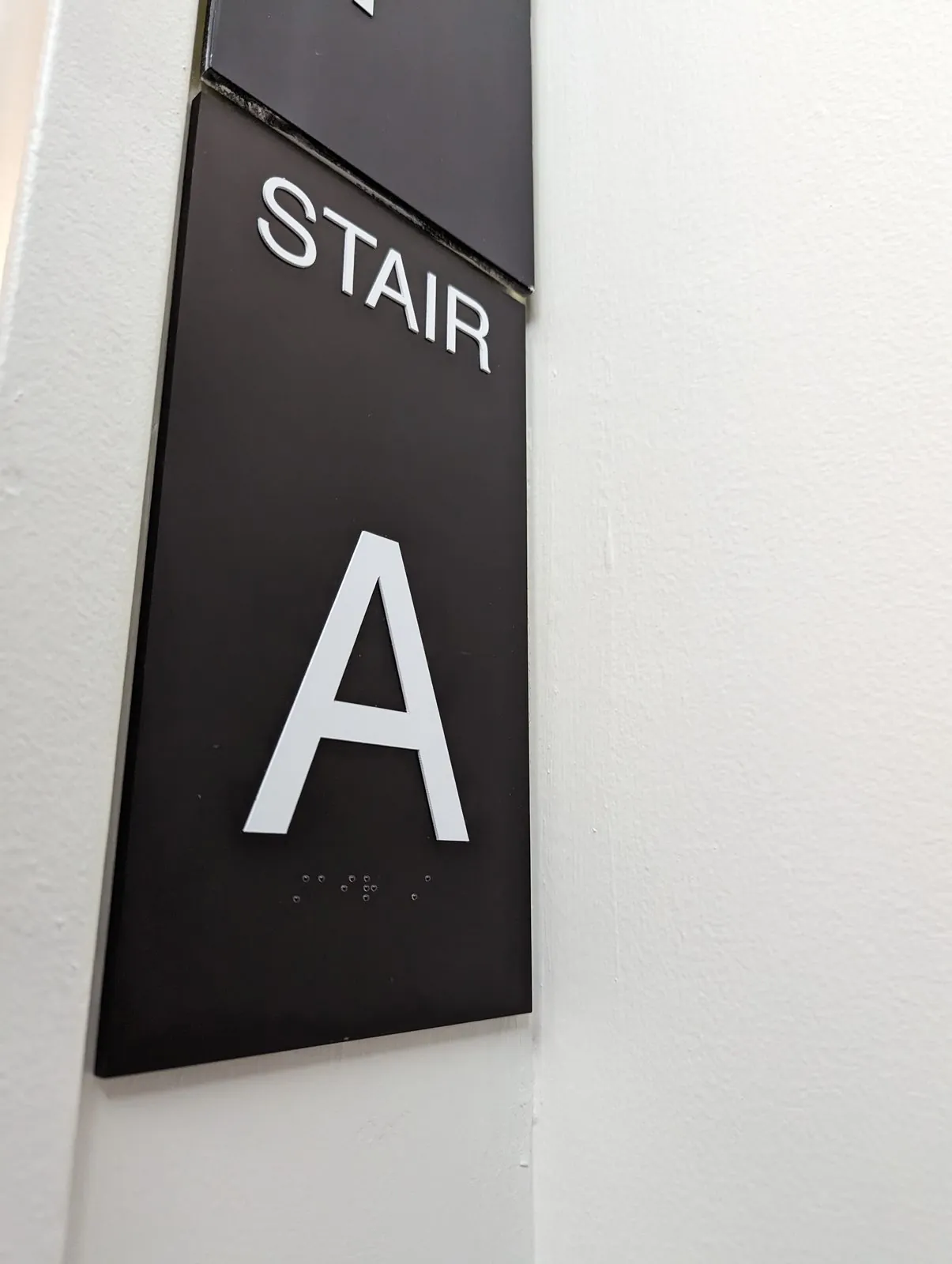 Black Stair A sign with raised white letters and braille on a white wall