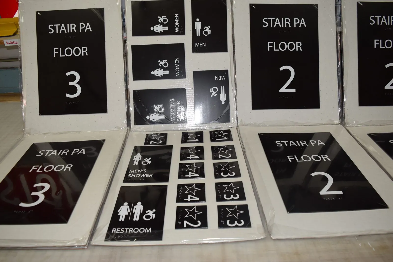A full set of Stair PA floor signs and restroom signs laid out on a shop table