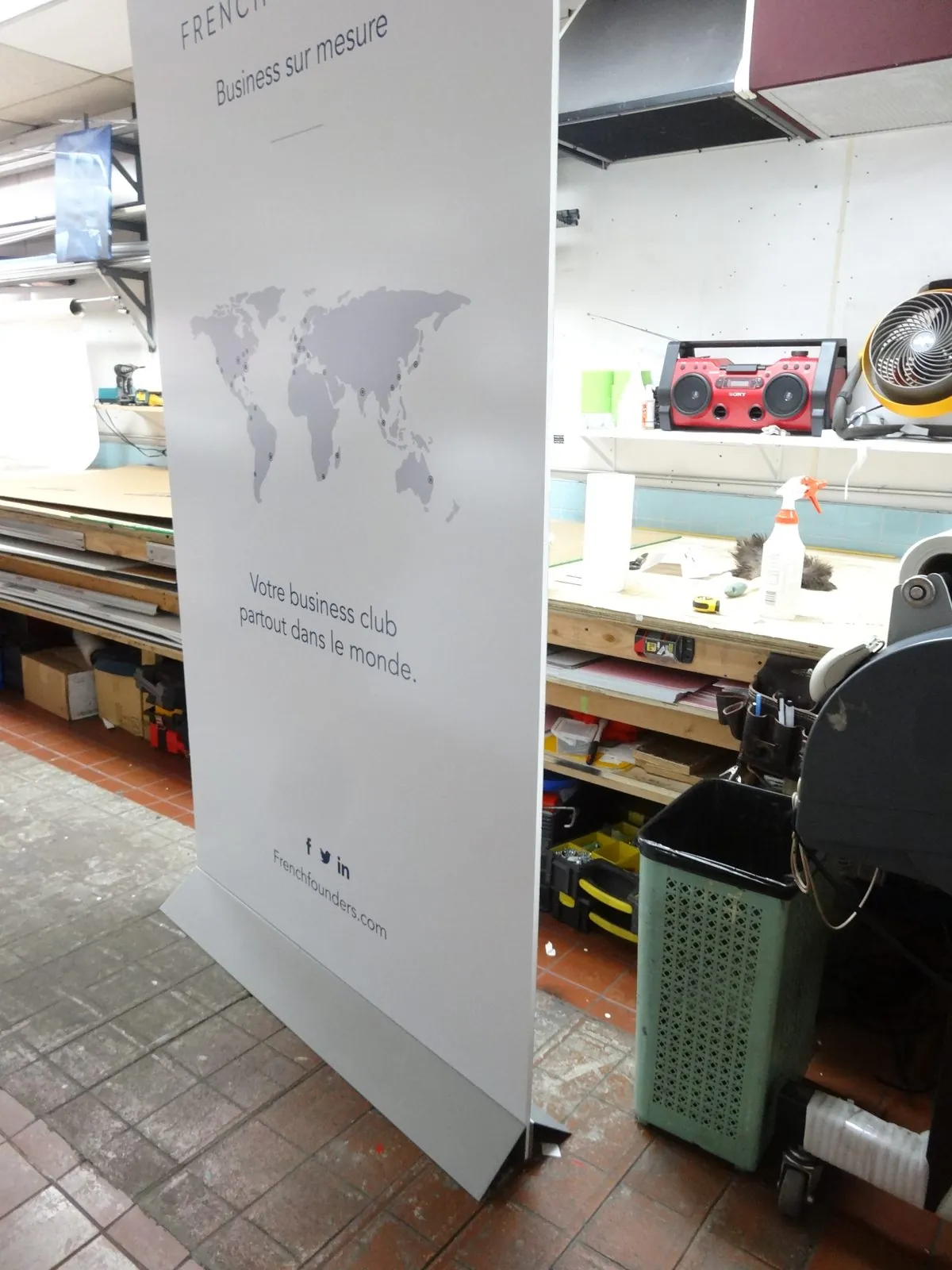 Tall white freestanding display with a gray world map graphic, standing on a metal foot in our shop