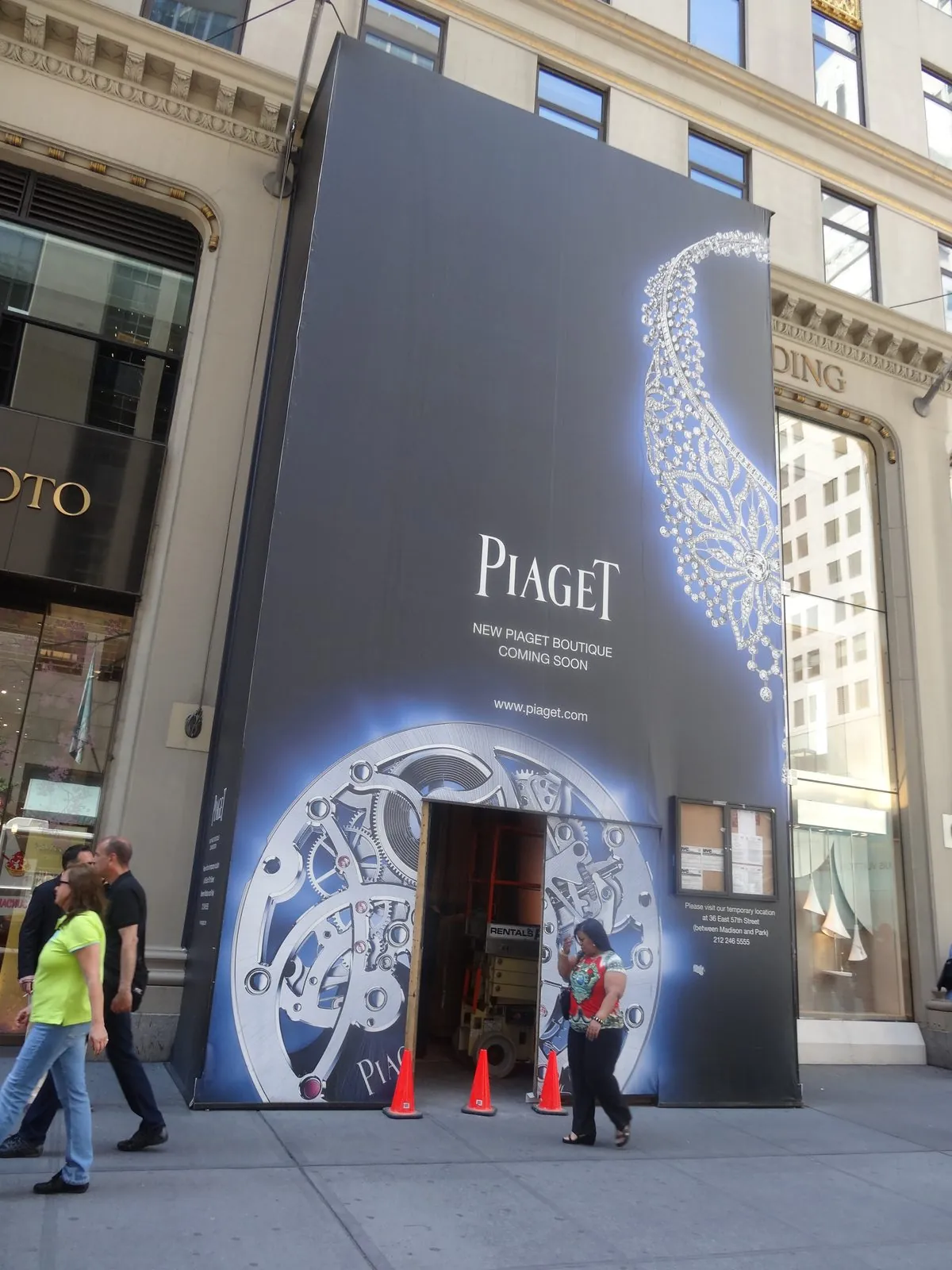 Tall printed barricade wall with a watch graphic around a store entrance under construction