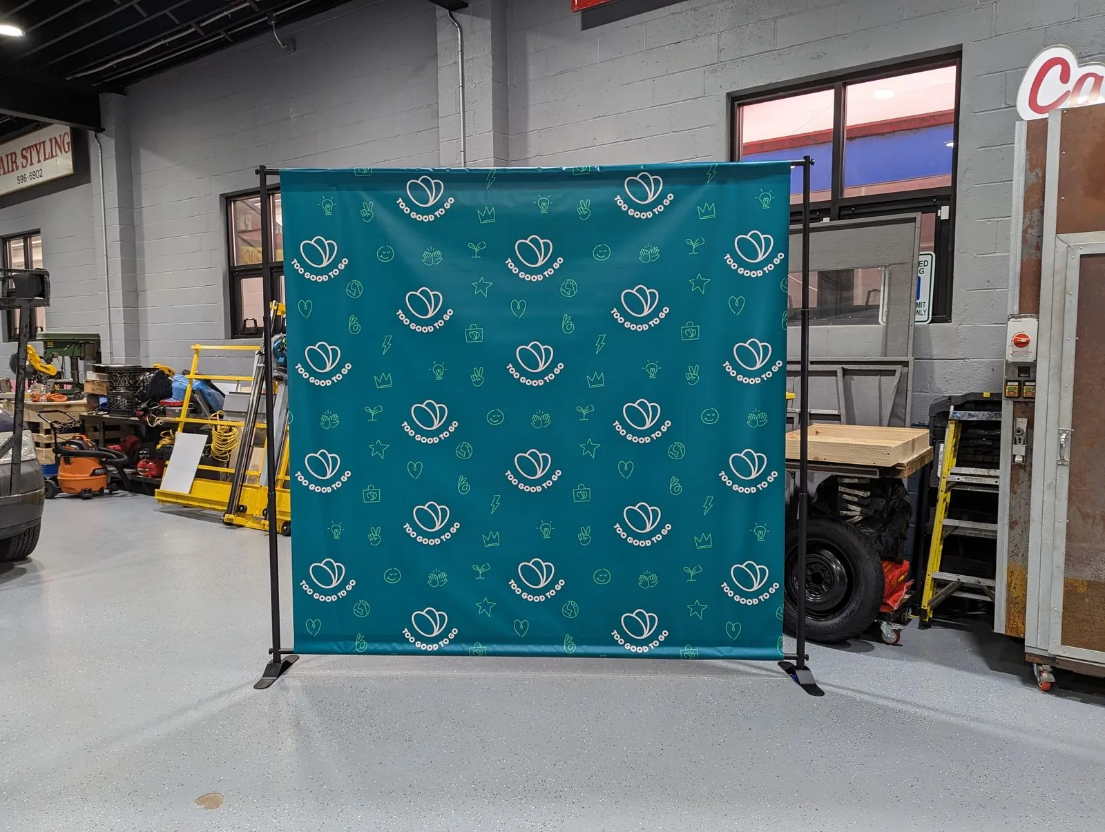 Teal step and repeat backdrop with a repeated white logo pattern on a black frame in our shop