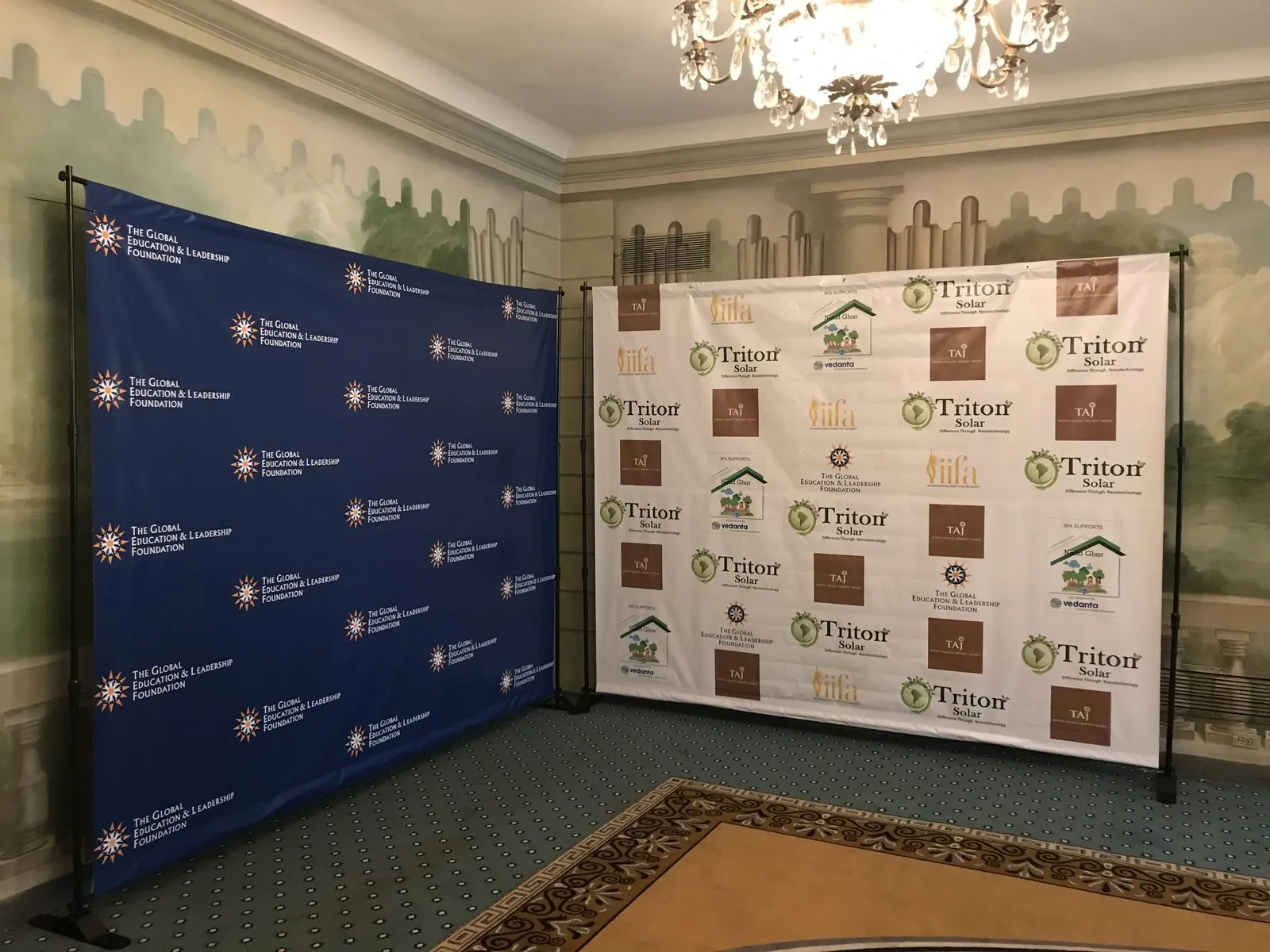 Two step and repeat backdrops on frames in the corner of a ballroom, one navy with white logos and one white with color logos